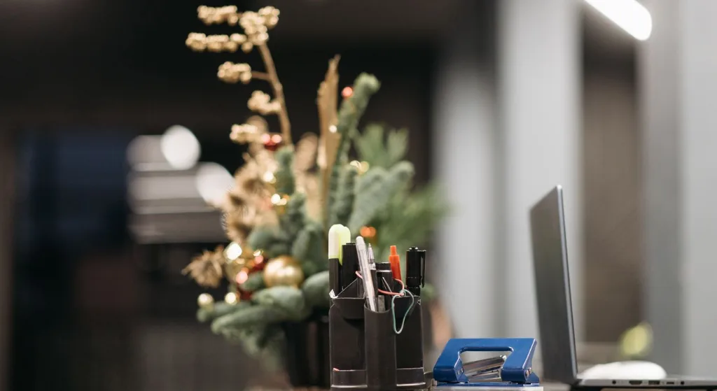 Office desk with holiday decorations, featuring a laptop, pens, and Christmas foliage