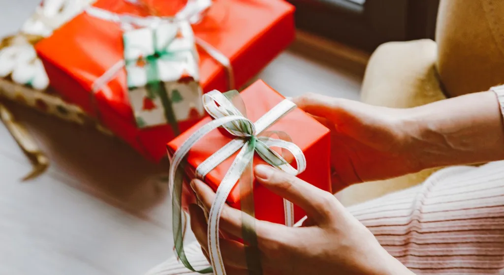Close-up of hands holding a wrapped Christmas gift tied with ribbon, capturing the festive mood